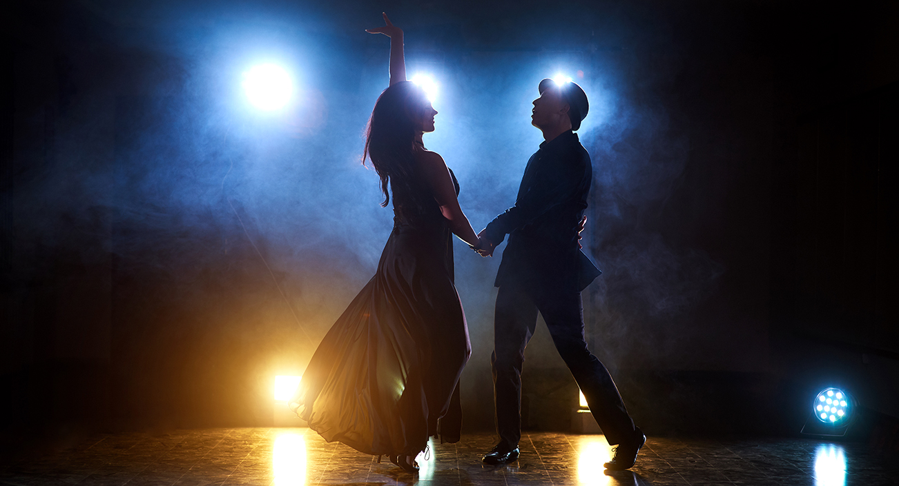 Skillful dancers performing in the dark room under the concert light and smoke. Sensual couple performing an artistic and emotional contemporary dance.